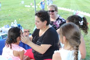woman face painting little girl while others watch
