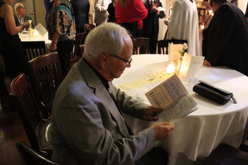 Man sitting at table with a glass of wine looking through the program of events for Vin Le Soir