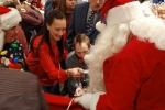 Group of people surrounding Santa as he hands out gifts from a bag at the Holiday Tea