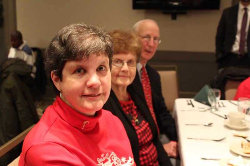 Woman with mother and father behind her smiling at the Holiday Tea event