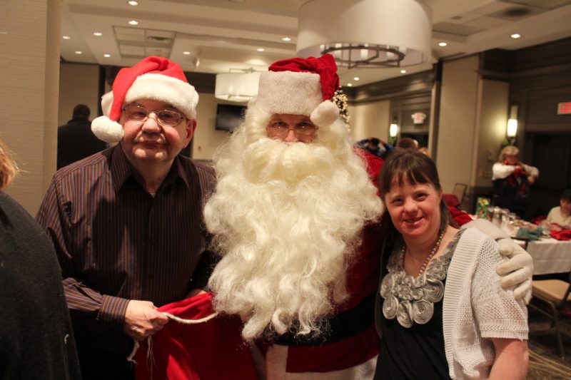 Two people smiling with Santa at the Holiday Tea event