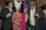 Four people smiling with feather masks on at Mardi Gras for AIM Services