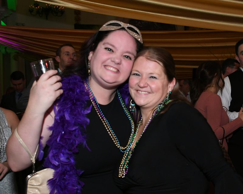 Two women with beads smiling at Mardi Gras event for AIM Services