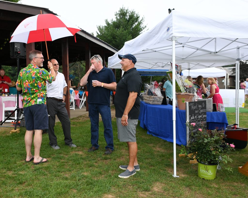 Group of men standing around with an umbrella at AIM Services Croquet on the Green event