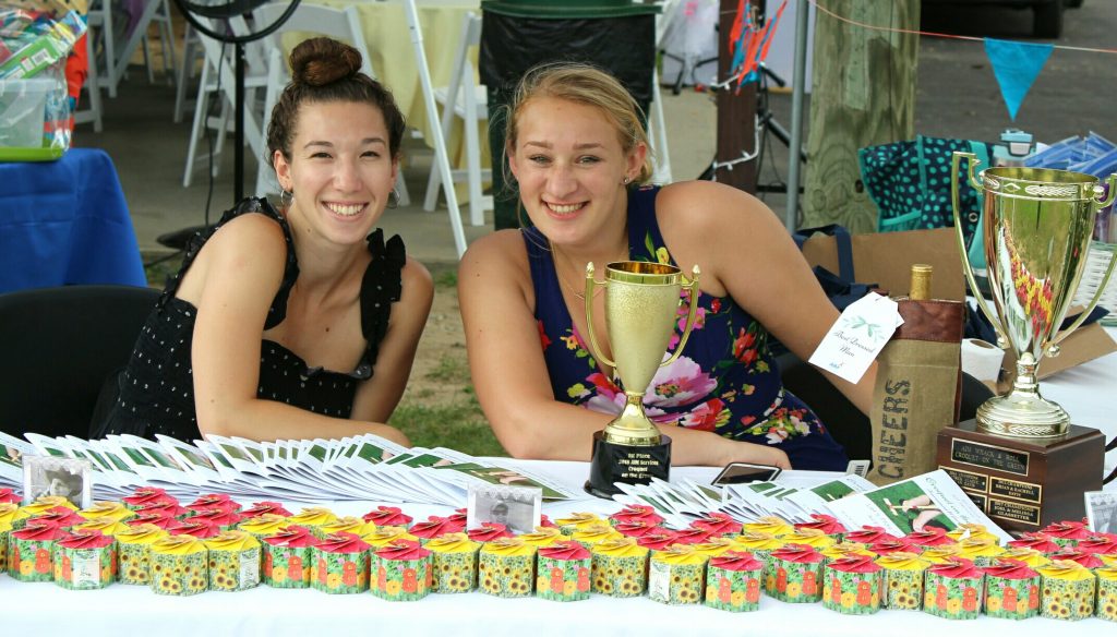 Two woman smiling at table with flower boxes at AIM Services Croquet on the Green event