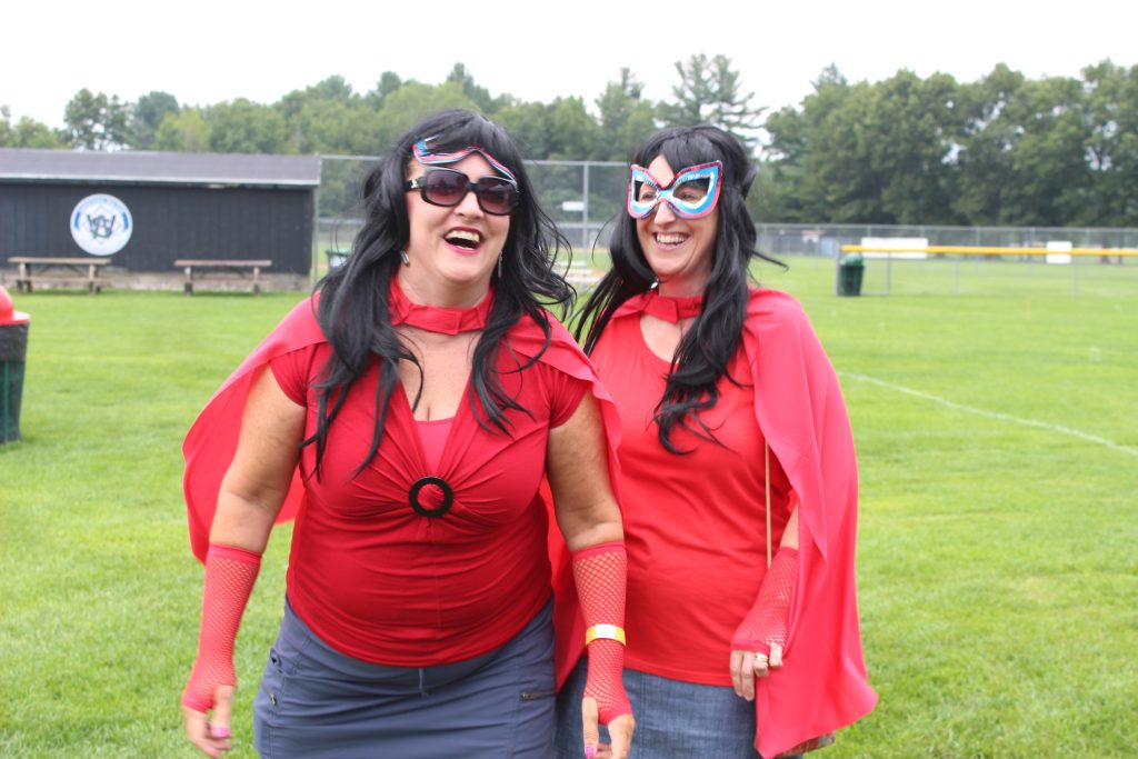 Two woman in superhero costumes laughing at AIM Services Croquet on the Green event