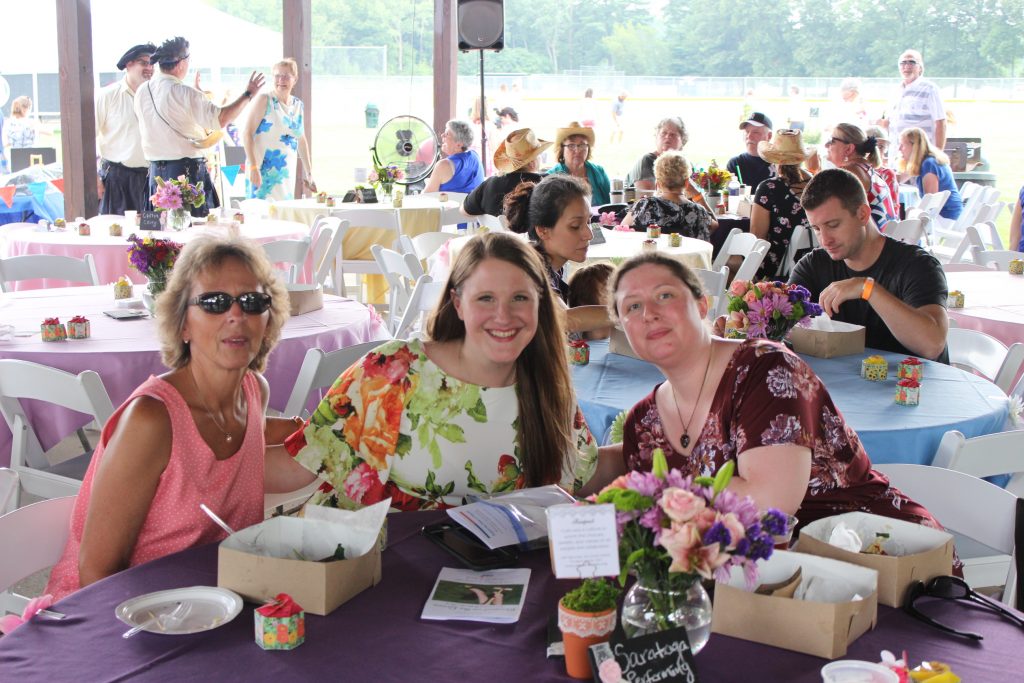 Three woman sitting at a table smiling at the camera at AIM Services Croquet on the Green event