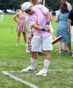 Man in pink shirt and knee high socks hitting croquet ball