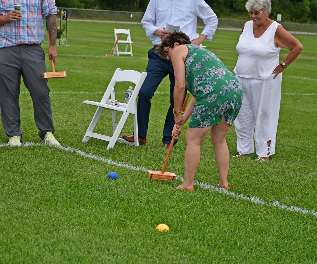 Woman in green dress bent over to hit croquet ball at Croquet on the Green 2019