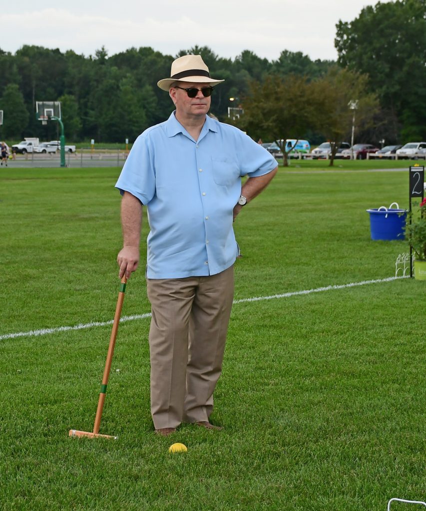 Man in light blue shirt with tan hat standing with croquet mallet at Croquet on the Green 2019