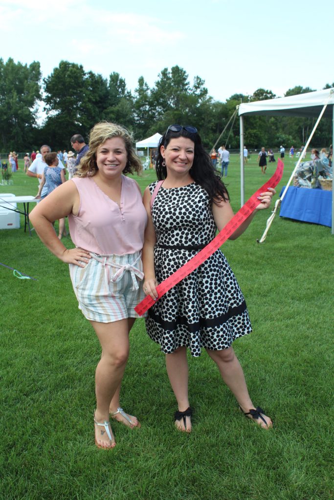 AIM staff Meghan Montayne and Sarah Papenhausen posing with a long strip of red raffle tickets at Croquet on the Green 2019