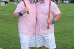 Two men in matching pink shirts, white pattern shorts, pink argyle socks, and white hats at Croquet on the Green 2019