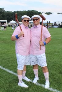 two men in matching pink and white outfits holding croquet mallets over their shoulders
