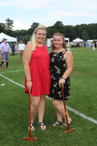 One young woman in red dress and one young woman in black pattern dress posing together with croquet mallets
