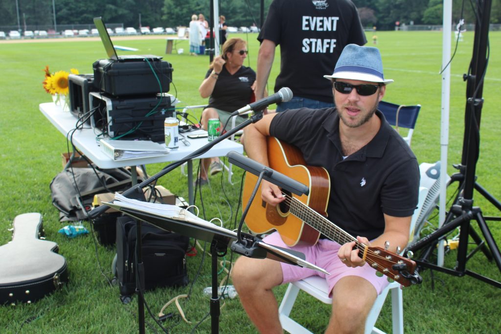 Thomas Powers looking at the camera singing while holding a guitar at Croquet on the Green 2019