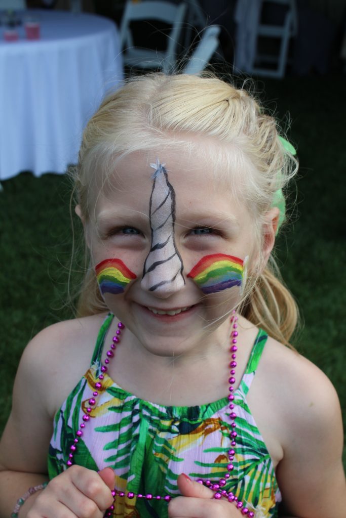 Young blonde girl with unicorn horn and rainbow face paint at Croquet on the Green 2019