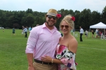 Woman in floral off the shoulder dress with pink flower in her hair smiling and holding her boyfriend with pink shirt and pink flower in his fedora hat at Croquet on the Green 2019