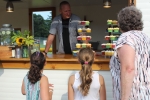 Older woman with two young girls looking at stacks of cupcakes as a man behind the counter looks on at Croquet on the Green 2019