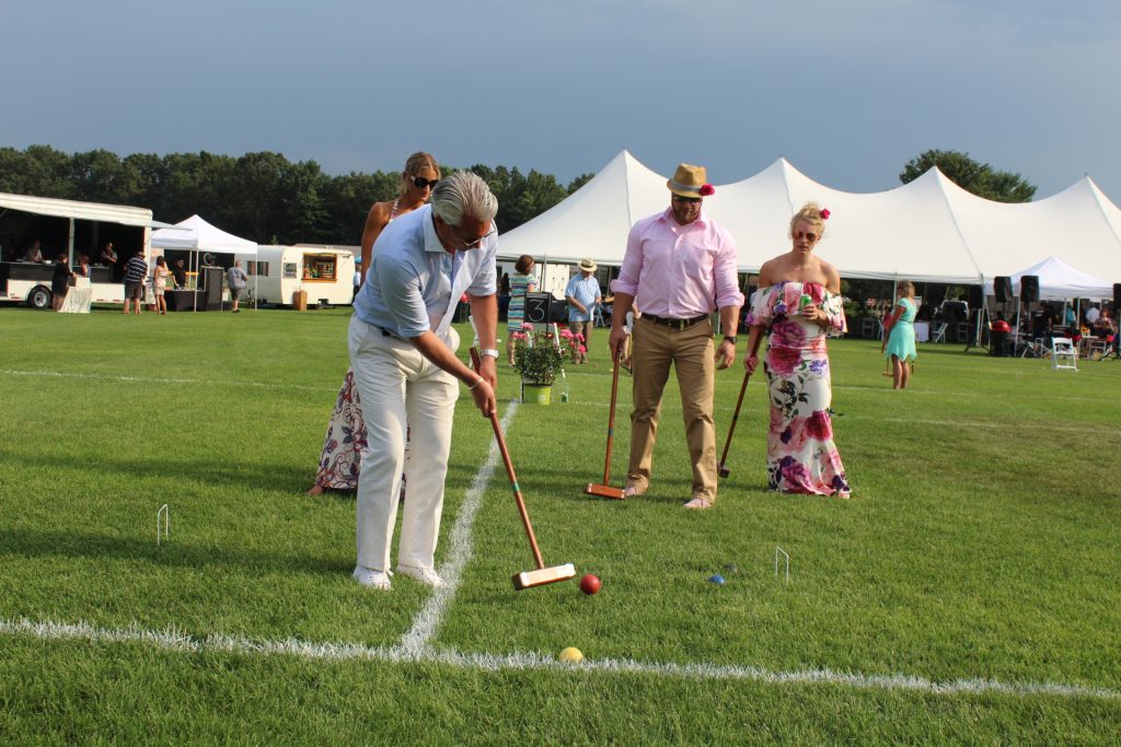 Man hitting croquet ball as group of three people look on at Croquet on the Green 2019