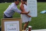 Woman holding high score sign for cornhole while a man points at his place on the board at Croquet on the Green 2019