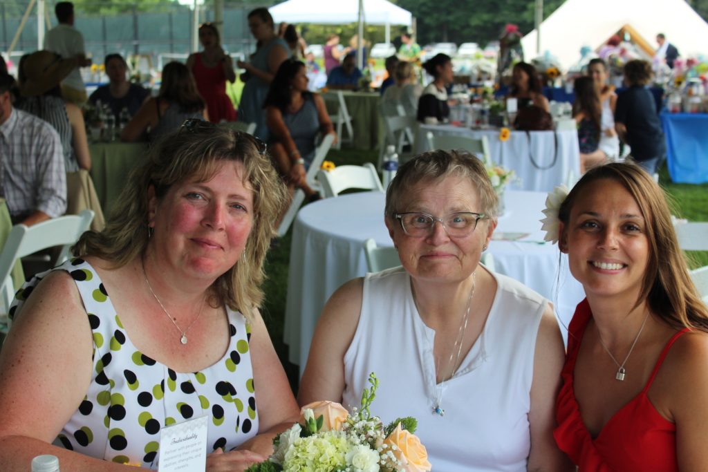 L-R: Noelle Fortier, June MacClelland, and Marissa Romero sitting at a table together smiling at Croquet on the Green 2019