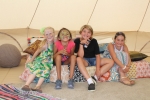 Group of four young girls sitting on bed in glamping tent at Croquet on the Green 2019