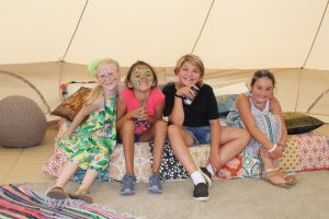 group of four young children smiling and sitting inside a tent