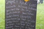 Black board sign with white lettering showing list of in-kind donors such as GlampADK, DeCrescente Distributing, ProNails and more at Croquet on the Green 2019