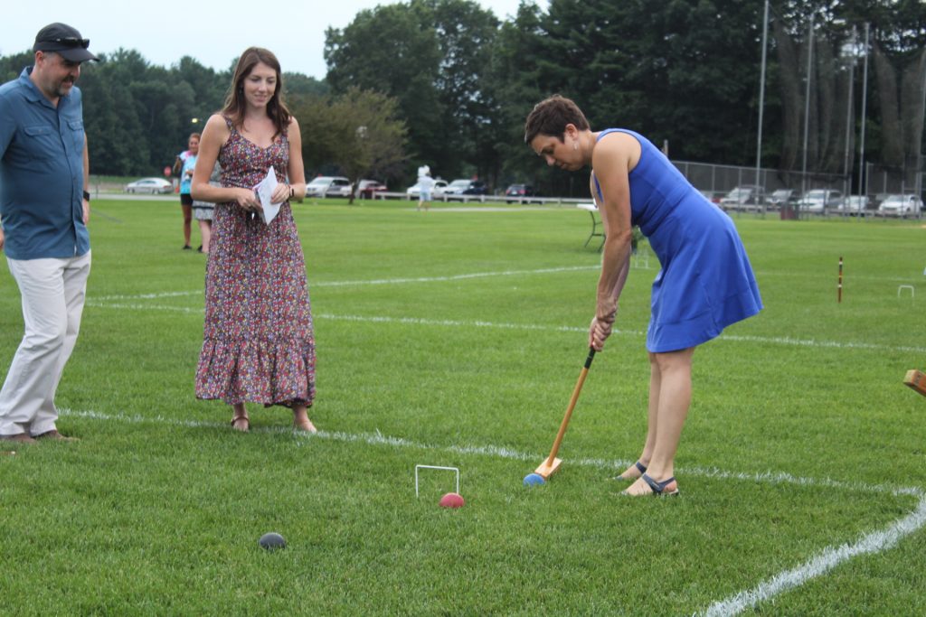 Woman in a blue dress taking a shot at croquet while two people look at at Croquet on the Green 2019