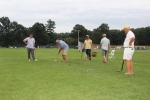 Man taking a shot at croquet as team mate, opponents, and croquet expert watches on at Croquet on the Green 2019