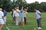 Man throwing his hands into the air while two other men high five in the background at Croquet on the Green 2019