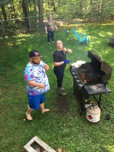 man in tie-dye shirt with woman sticking her tongue out and giving thumbs up in front of a bbq grill