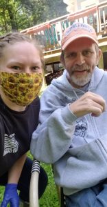 Woman with yellow patterned mask taking a selfie with an older man in a grey zip-up hoodie