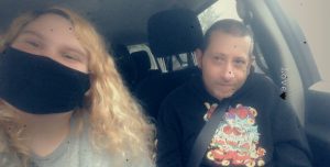 women with curly blonde hair wearing mask in car with older man
