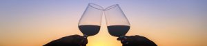 Image of two wine glasses cheersing over sunset