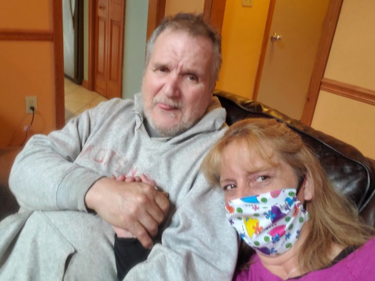 woman in colorful face mask holding hands with older man in a grey sweatshirt