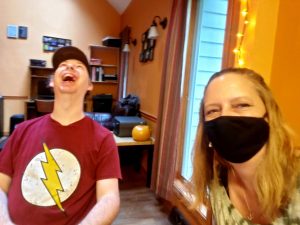 woman with black mask sitting next to man with lightning bolt in his shirt and throwing his head back in laughter