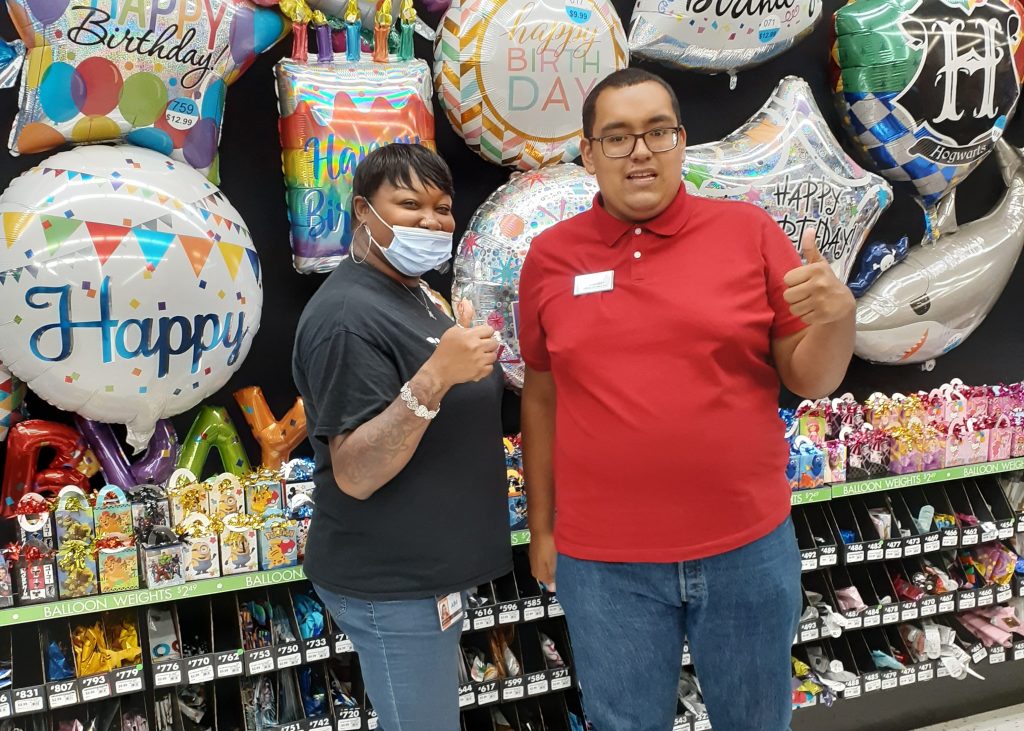 woman and man giving a thumbs up standing in front of a wall of party balloons