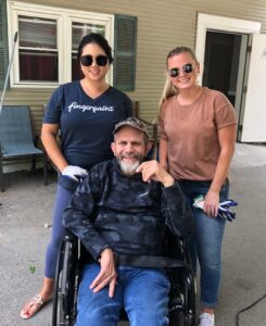 two woman standing with man in wheelchair in front of a house
