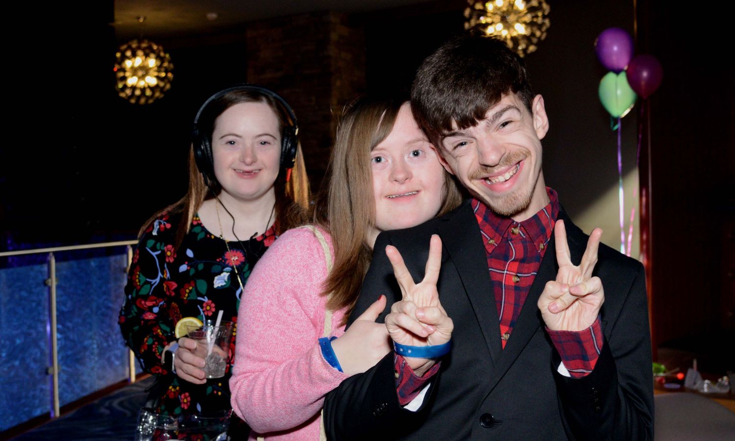 Three people together, one holding up peace signs and another wearing headphones