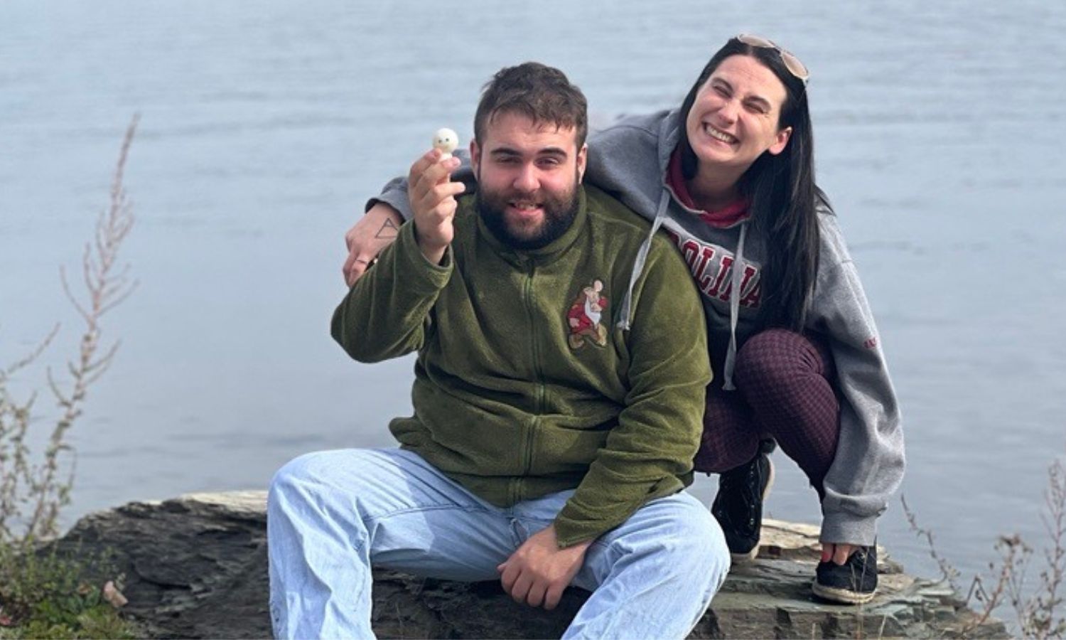 Two people smiling sitting on a rock