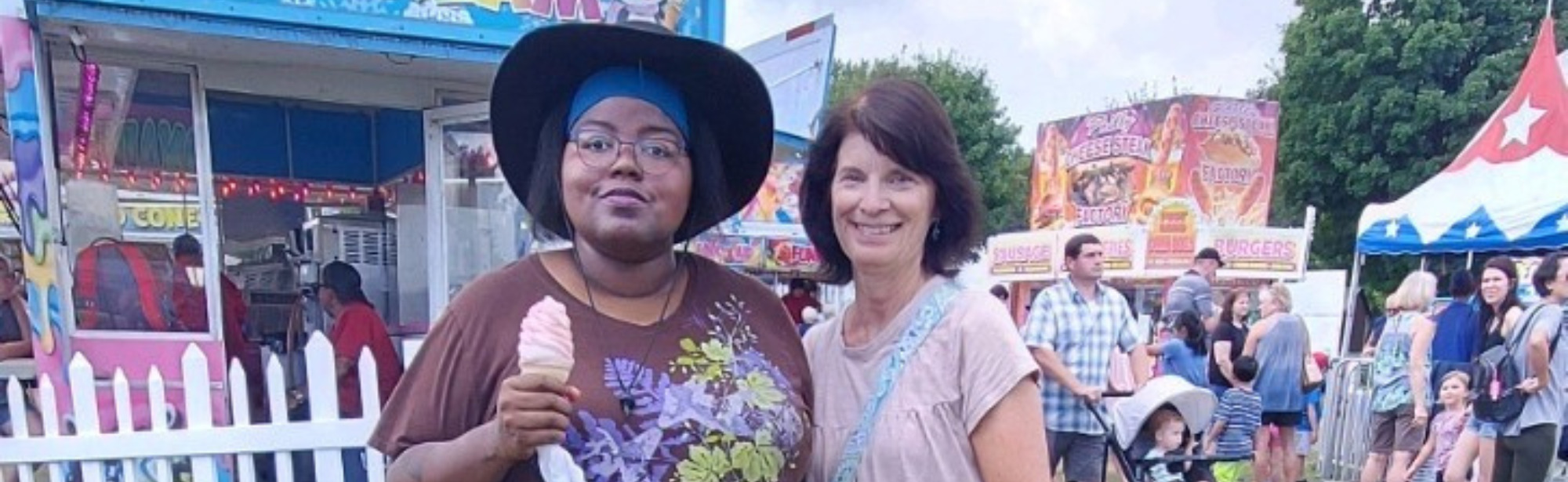 two people at an outdoor fair, one is holding ice cream